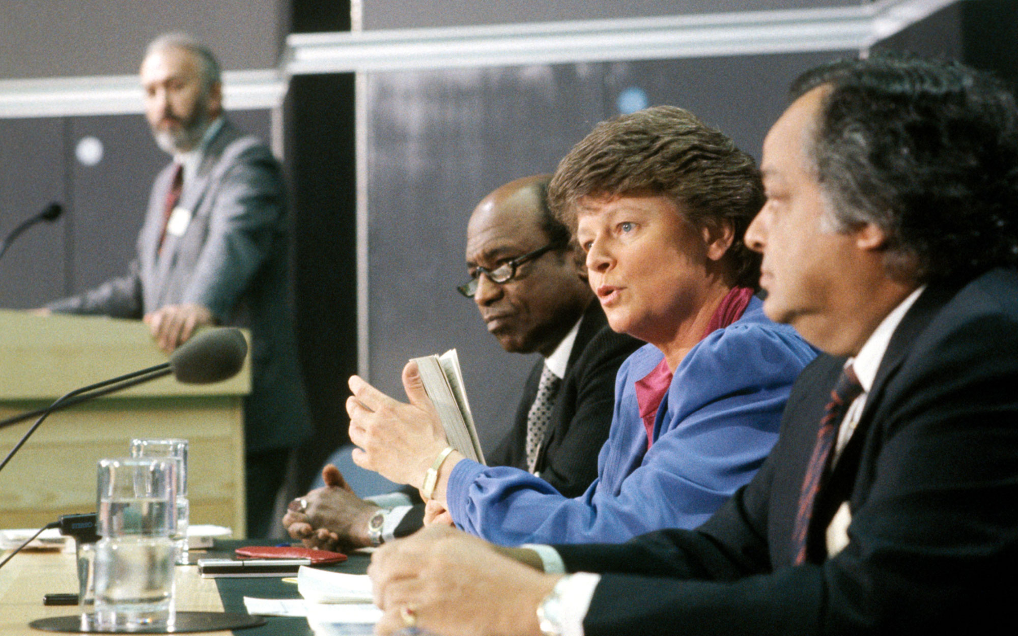 Bilde av Gro Harlem Bruntland fra Brundtlandkommisjonen. Bruntland sitter ved et bord og snakker i en mikrofon.